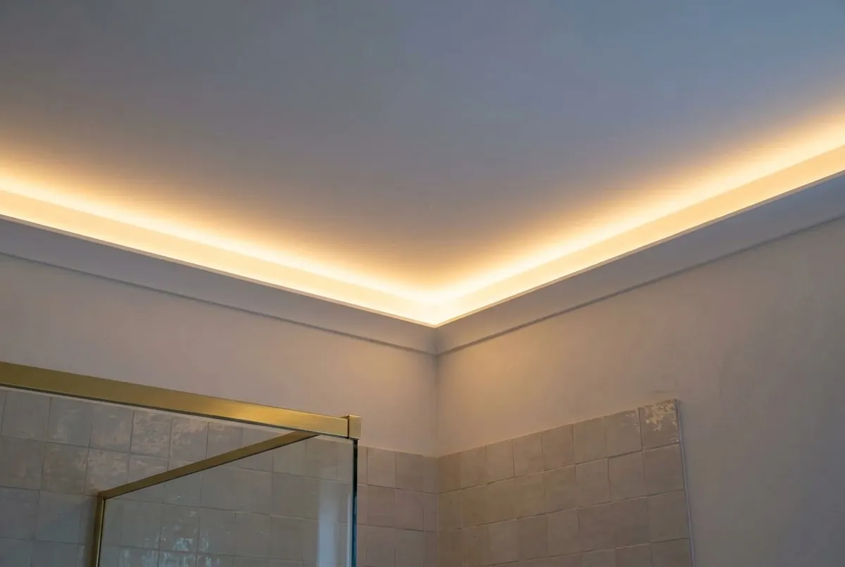 AI-impressie van een badkamerplafond met een verlaagde rand waarachter een verborgen ledstrip een gelijkmatige warme gloed over het witte plafond geeft, boven een getegelde wand en een douchewand