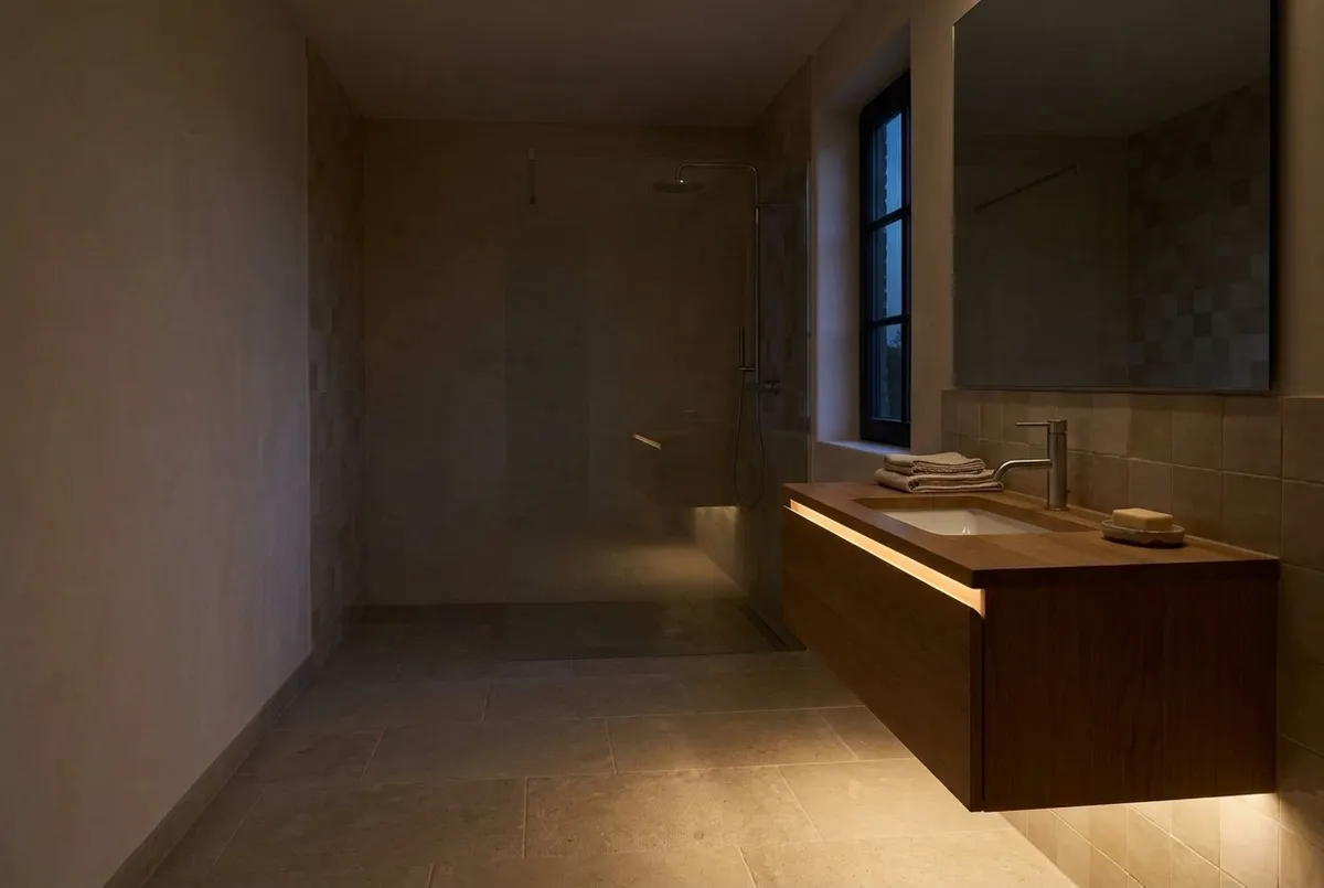 AI-impressie van een donkere badkamer waar alleen een zwakke ledstrip onder het zwevende wastafelmeubel de vloer verlicht