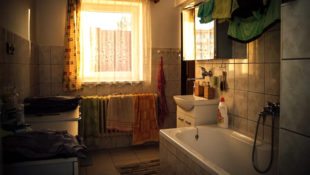 Gedateerde badkamer met oude wandtegels, een ligbad en handdoeken aan de radiator, het startpunt van een verbouwing