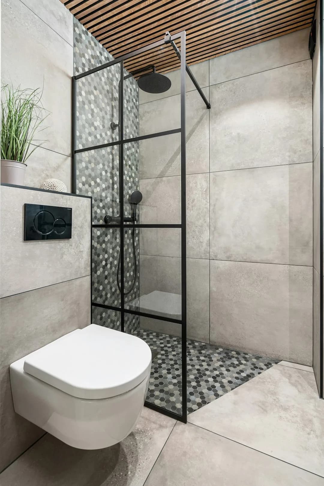 Kleine badkamer met een inloopdouche achter één vast glaspaneel in zwart profiel, naast een hangend toilet en een douchevloer van hexagon mozaïek
