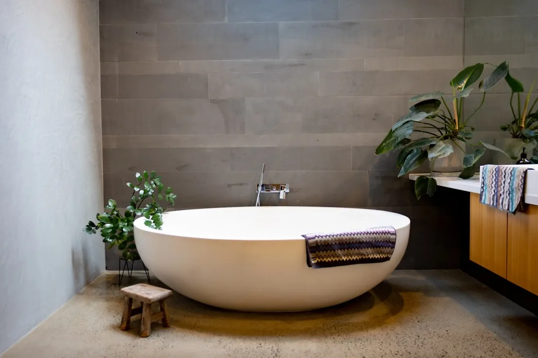 Badkamer met vrijstaand bad, natuurstenen vloer en een grote plant in de hoek
