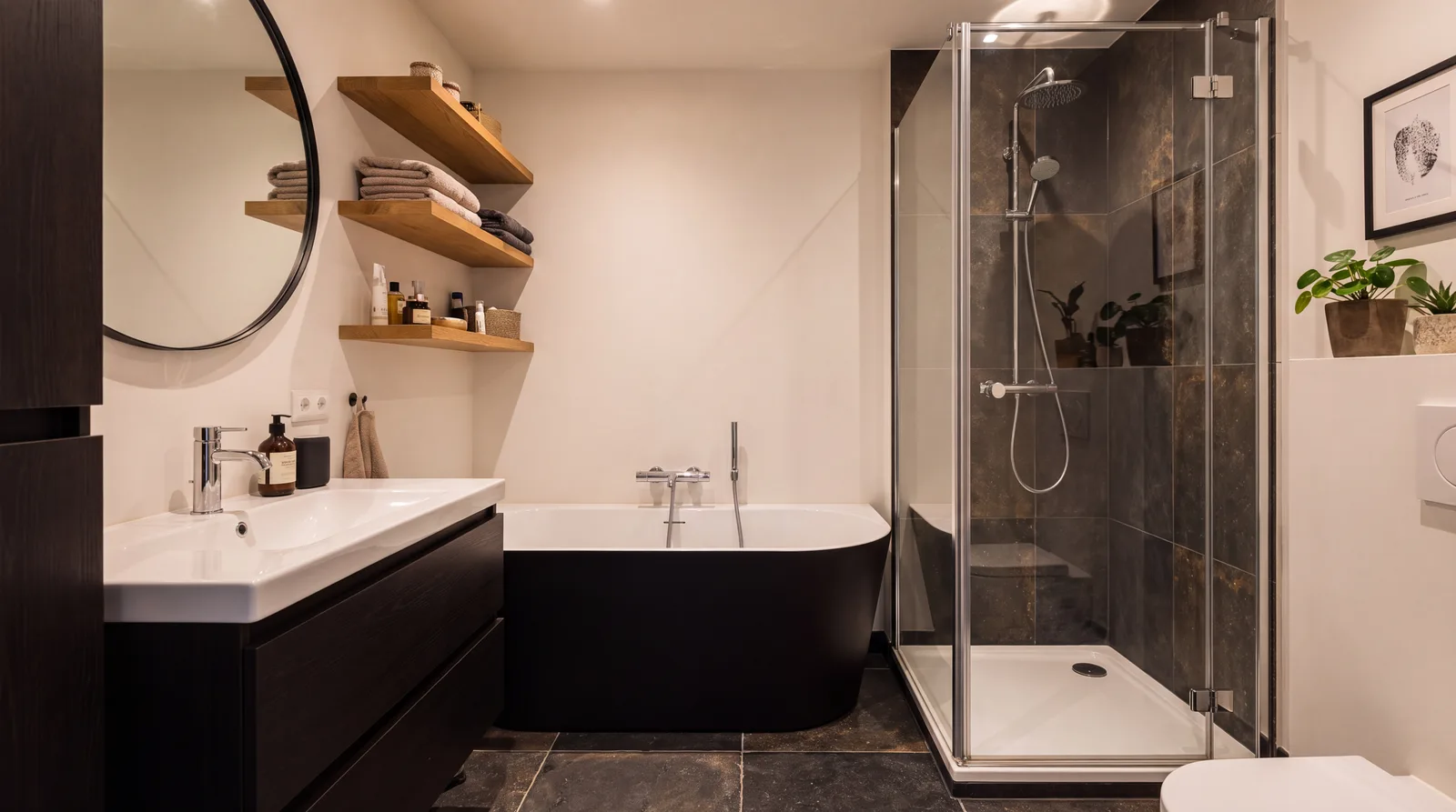 Zwart bad tussen een wastafelmeubel en een douchehoek in een smalle badkamer