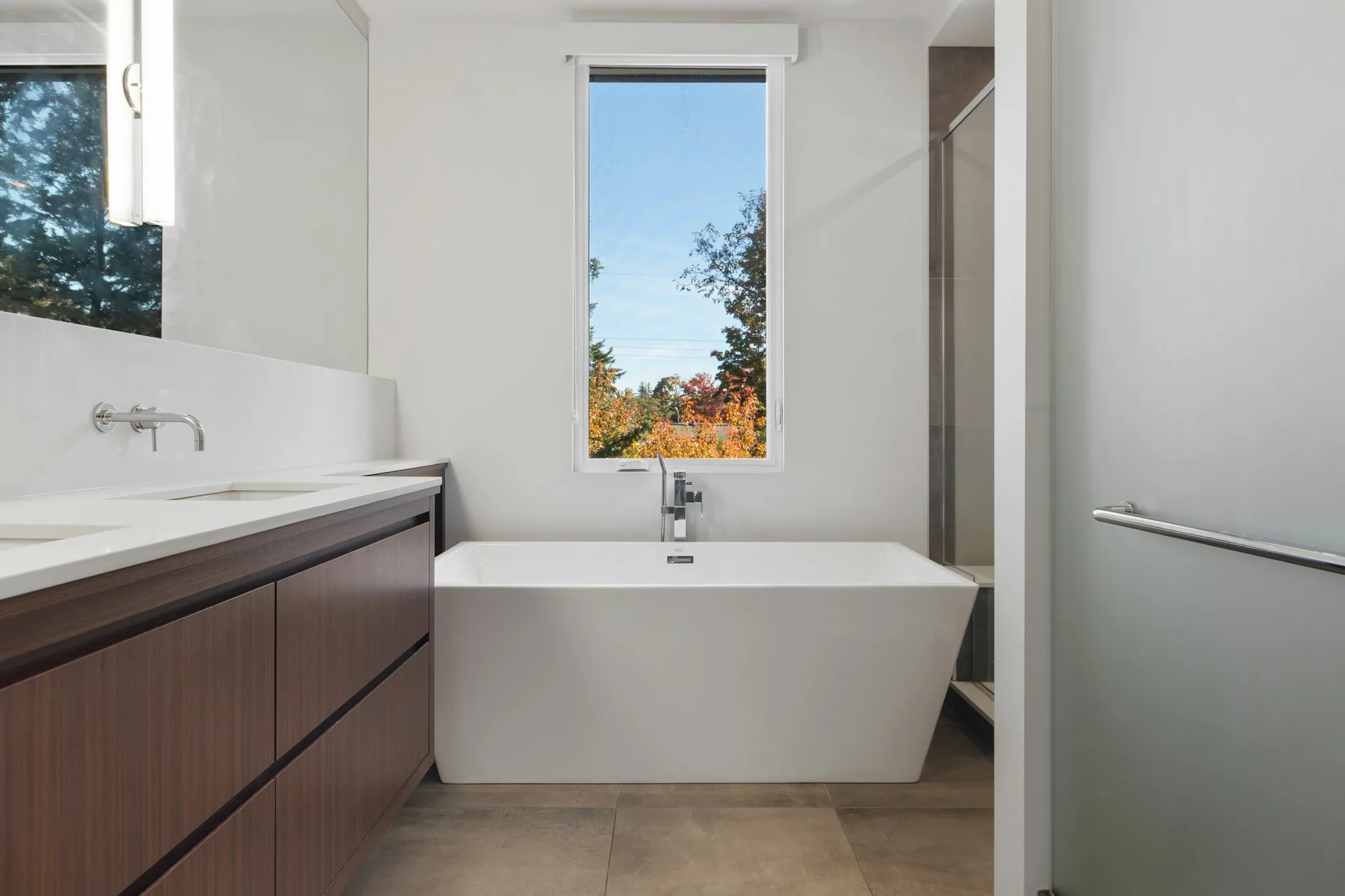 Badkamer met een donker houten badmeubel, wandkraan en vrijstaand bad voor een hoog raam