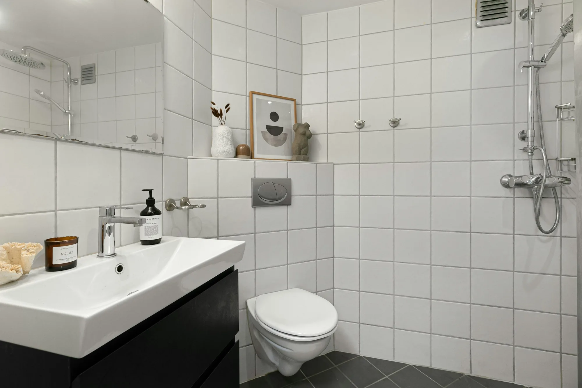 Badkamer met witte wandtegels, een donkere vloer, een zwart wastafelmeubel en een hangtoilet