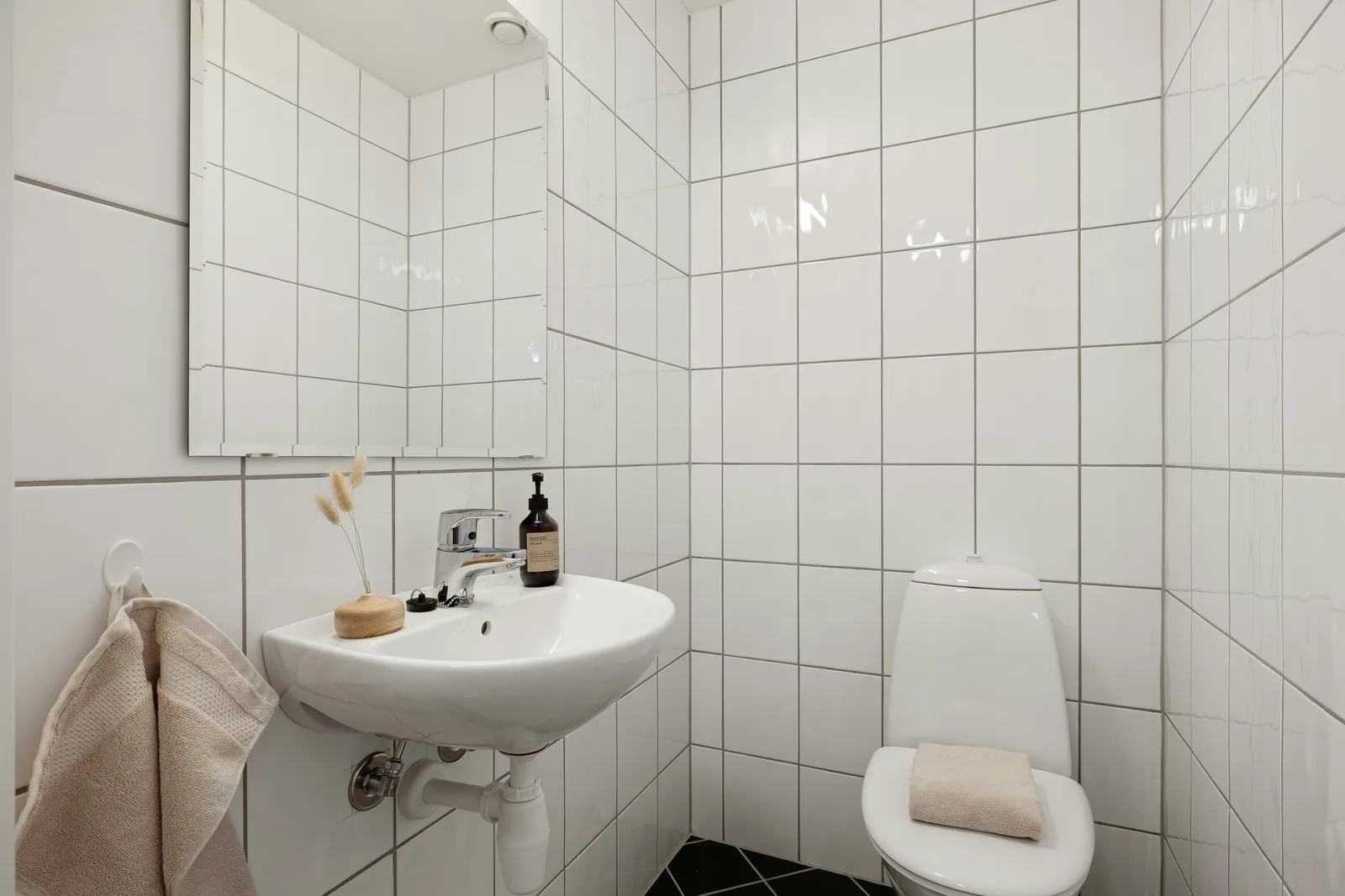 Wit betegelde toiletruimte met veel voeglijnen, een wandwastafel en een spiegel aan de wand
